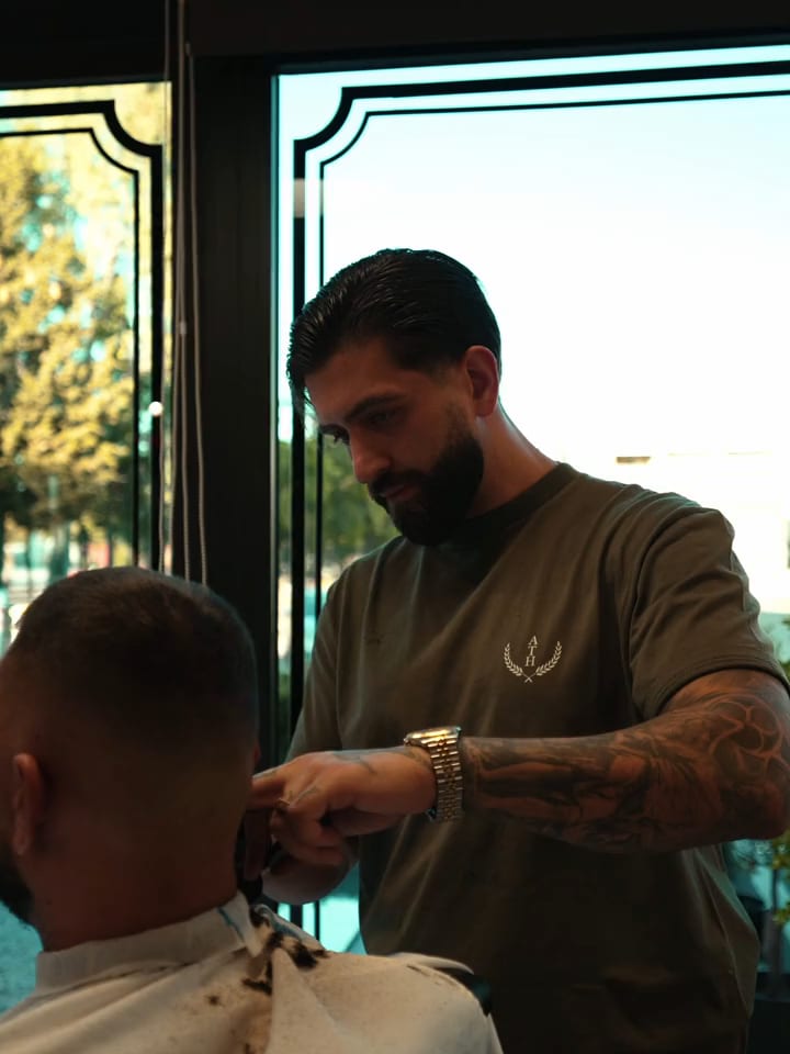 Barber του The Athenians κουρεύει πελάτη μπροστά στα τοξωτά παράθυρα του κουρείου